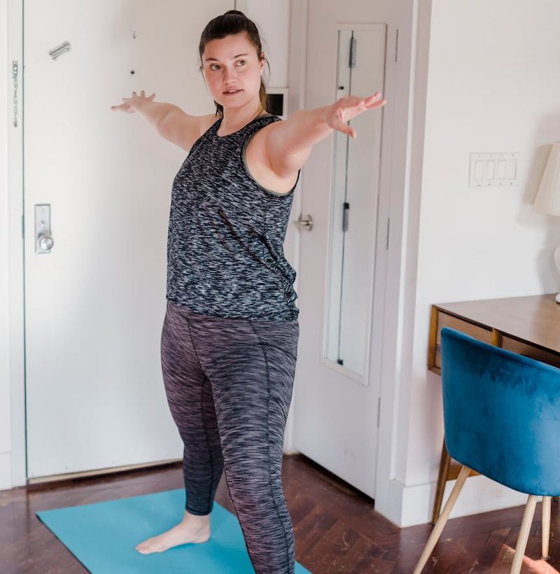 Person in a focused warrior yoga pose in a spacious, sunlit room.